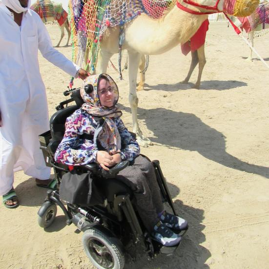 Anna i elektrisk kørestol med kamel i baggrunden