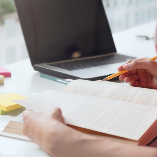 En kvinde, der læser i en bog. Ved siden af hende ses en computer og forskellige studieredskaber.