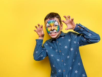 Et barn, med ansigtet malet som et dyr. De smiler med hænderne oppe som små kløer.