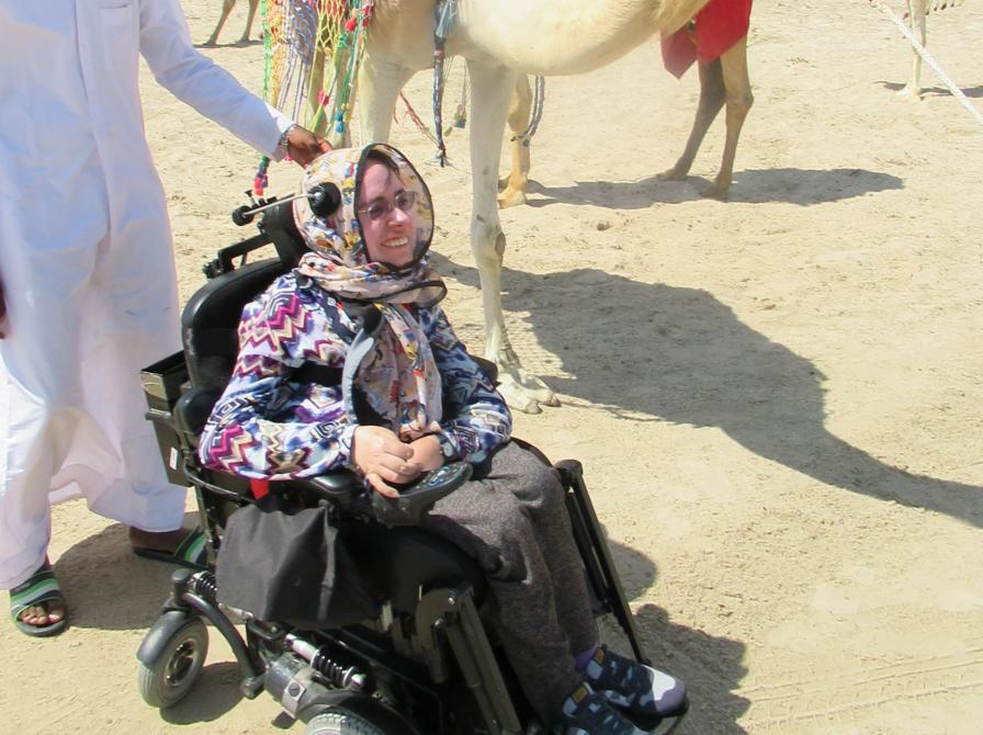 Anna i elektrisk kørestol med kamel i baggrunden