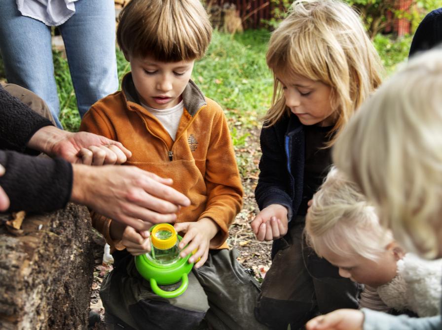 Barn, der sidder på jorden og kigger på et insekt med et forstørrelsesglas.